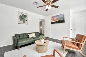 Una sala de estar moderna con un sofá verde, un sillón de cuero marrón y una mesa de centro redonda de madera.