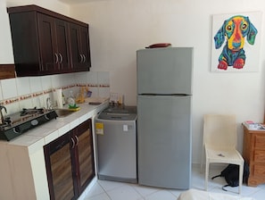 A kitchen with a stove, sink, and refrigerator. There is a chair and a painting on the wall. - APARTMENT WITH A PRIVATE TERRACE (Sosúa)