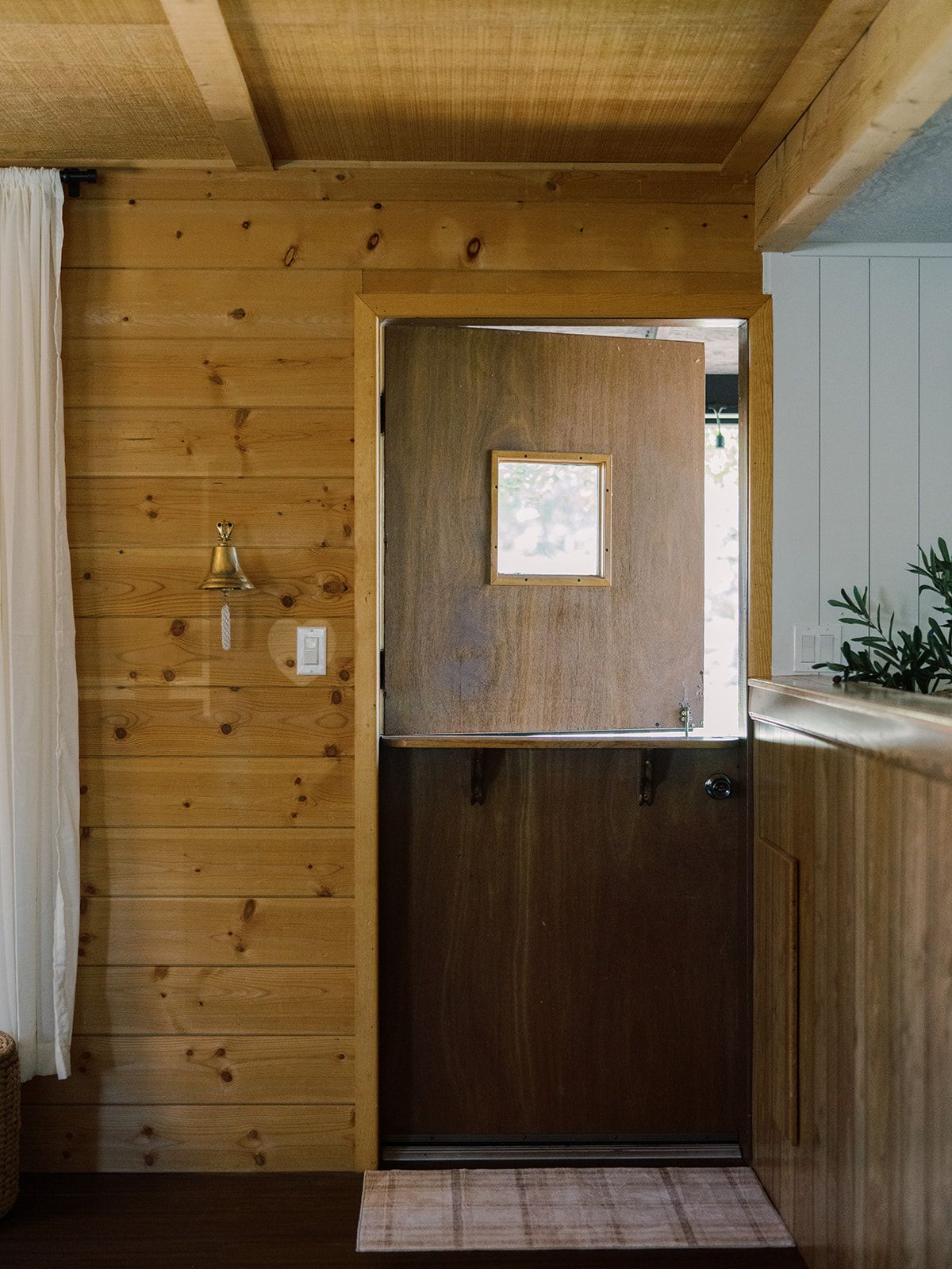 A wooden interior with a door, a small window, and a bell.