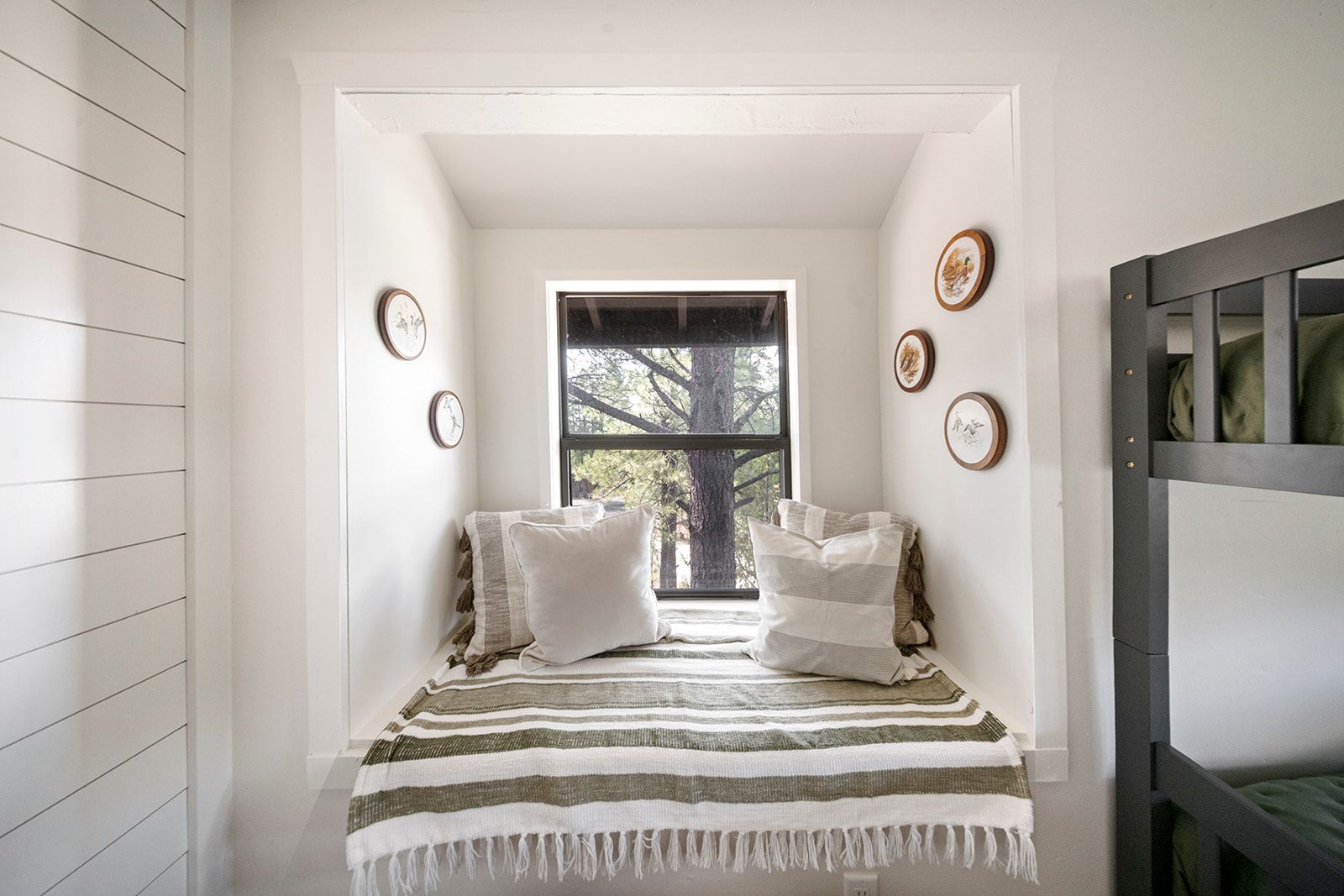 A narrow room with a window, a bed with striped bedding, and wall-mounted picture frames.