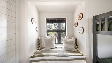 A narrow room with a window, a bed with striped bedding, and wall-mounted picture frames.
