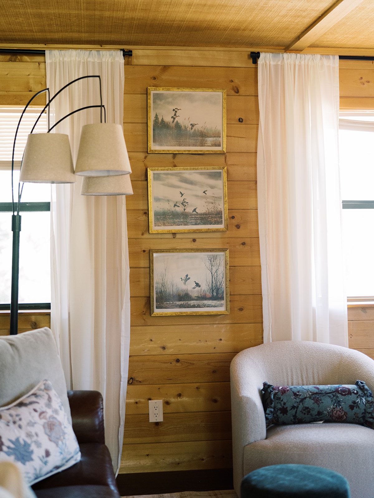 L’intérieur d’une cabane avec des murs en bois, un canapé, un fauteuil et trois tableaux encadrés accrochés au mur.