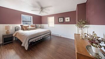 A bedroom with a bed, nightstand, lamp, ceiling fan, window, and wall-mounted pictures.