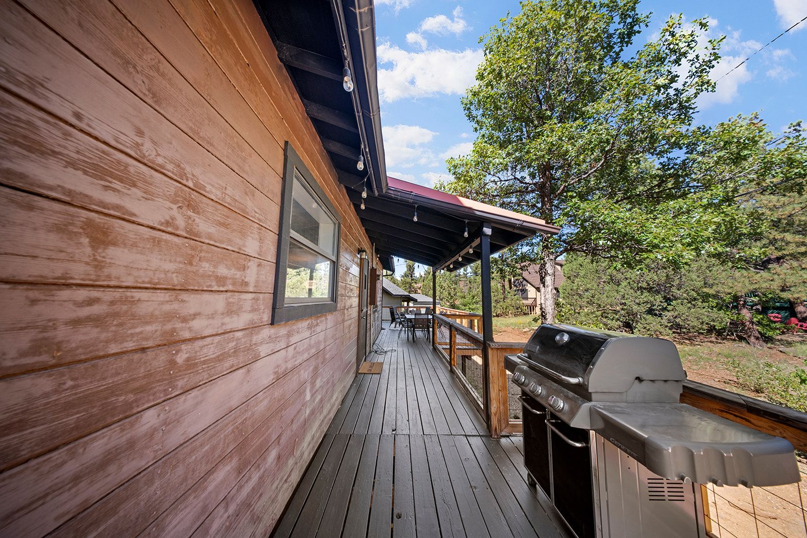 A wooden deck with a barbecue grill, a covered seating area, and a view of the surrounding landscape.