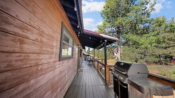 A wooden deck with a barbecue grill, a covered seating area, and a view of the surrounding landscape.