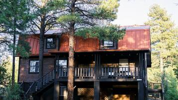A two-story cabin with a wooden exterior, a balcony on the upper floor, and a staircase leading to the entrance.