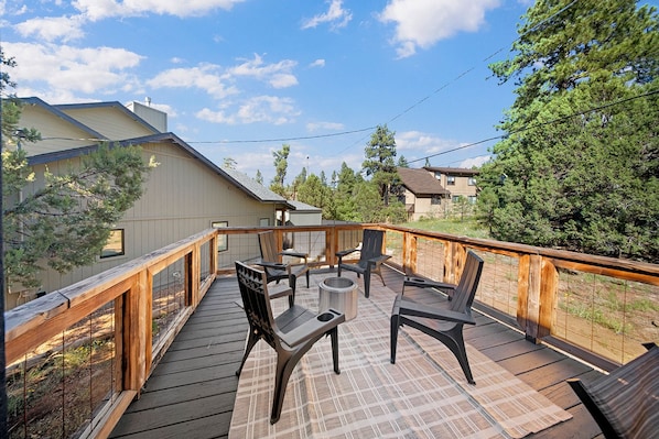 A deck with outdoor furniture and a fire pit, surrounded by a wooden railing.