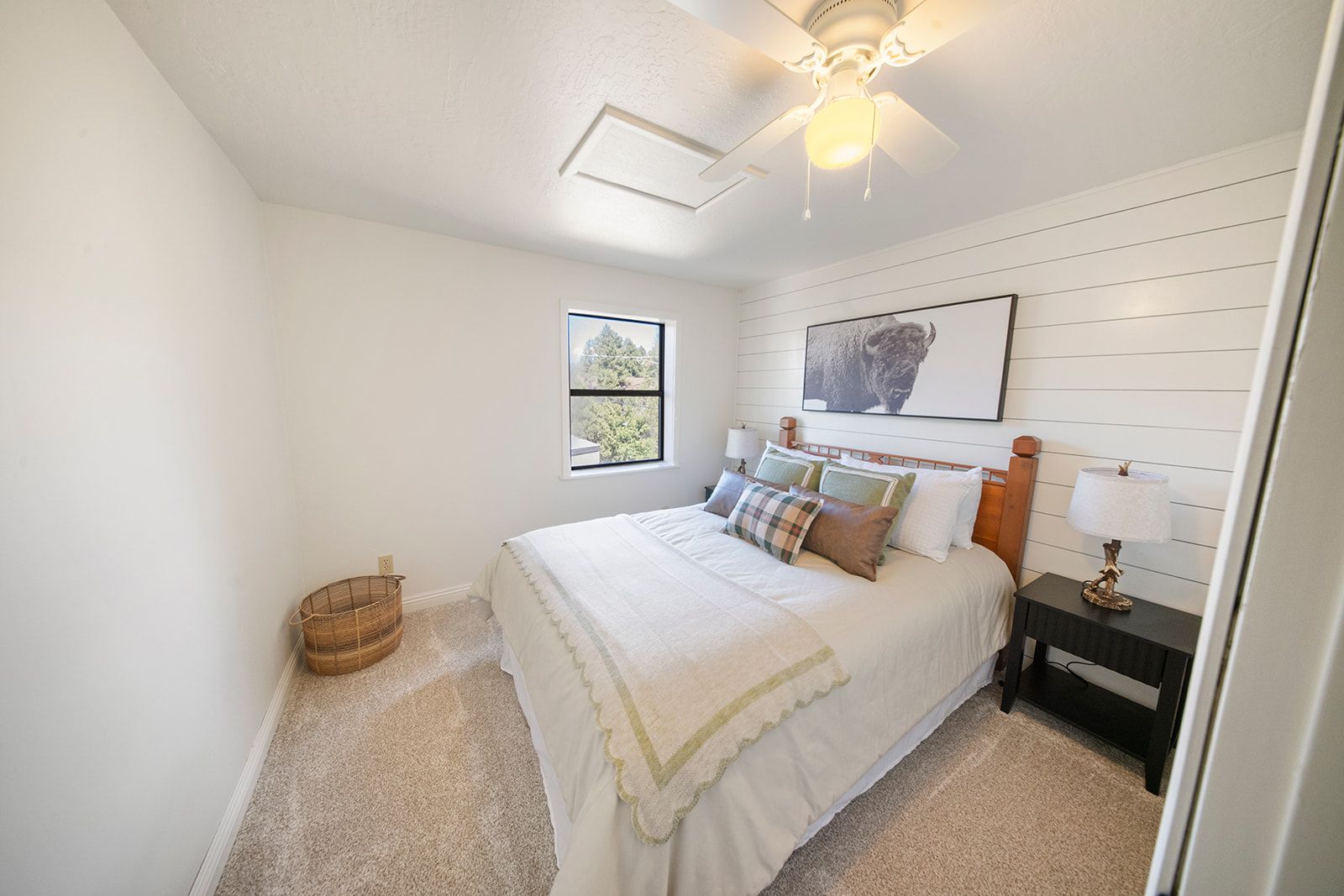 A bedroom with a bed, a nightstand, a lamp, a window, and a ceiling fan.