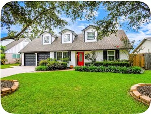 A two-story house with a red door, a garage, and a well-maintained lawn. - Houston Southwest Oasis – Heater Pool & Game Room (Houston)