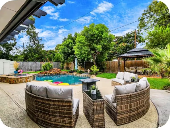 A backyard with a swimming pool, wicker furniture, and a covered patio area. - Houston Southwest Oasis – Heater Pool & Game Room (Houston)