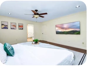 Ein Schlafzimmer mit einem Bett, einem Deckenventilator, einem Gemälde und einer Tür zu einem Badezimmer.