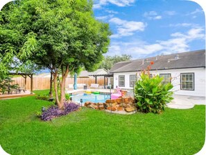 Ein Garten mit Swimmingpool, Baum und weißem Haus.