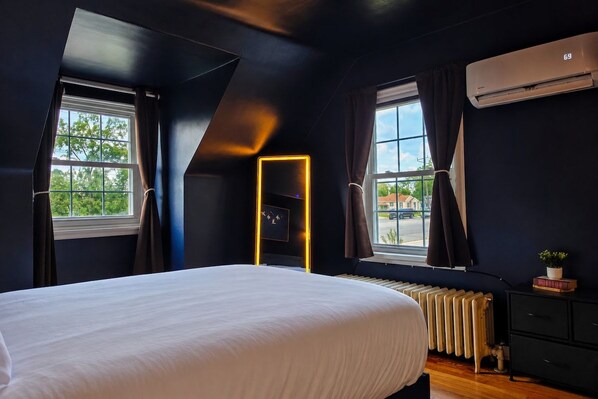 A bedroom with a large bed, a radiator, a window with curtains, and an air conditioning unit.