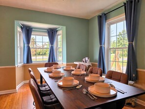 A dining room with a long table set for a meal, chairs, and a window with curtains.