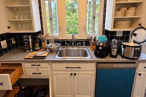 A kitchen with a stainless steel sink, a coffee maker, a blender, and a pot on the counter.