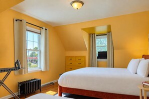 Ein Schlafzimmer mit einem Bett, einem Heizkörper, einem Fenster mit Vorhängen, einem Schminktisch und einem kleinen Tisch mit Büchern.