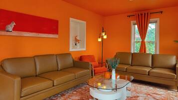 A living room with two brown leather sofas, a glass coffee table, and a red abstract painting on the wall.