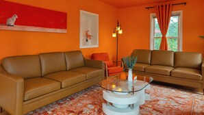 A living room with two brown leather sofas, a glass coffee table with candles, and a red abstract painting on the wall. - Coastal Home | Patio & Firepit | Backyard Games (Merrillville)