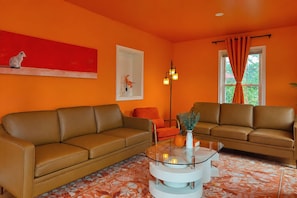 Ein Wohnzimmer mit zwei braunen Ledersofas, einem Glastisch mit Kerzen und einem abstrakten roten Gemälde an der Wand.
