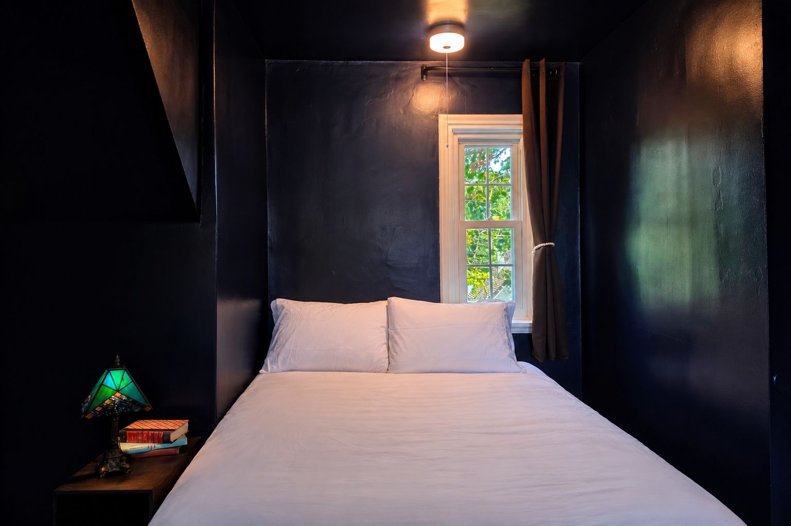 Ein Schlafzimmer mit einem Bett, einem Nachttisch mit Lampe und einem Fenster mit Vorhängen.