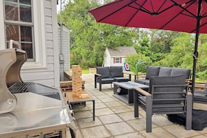 An outdoor patio with a grill, seating area, and a red umbrella.