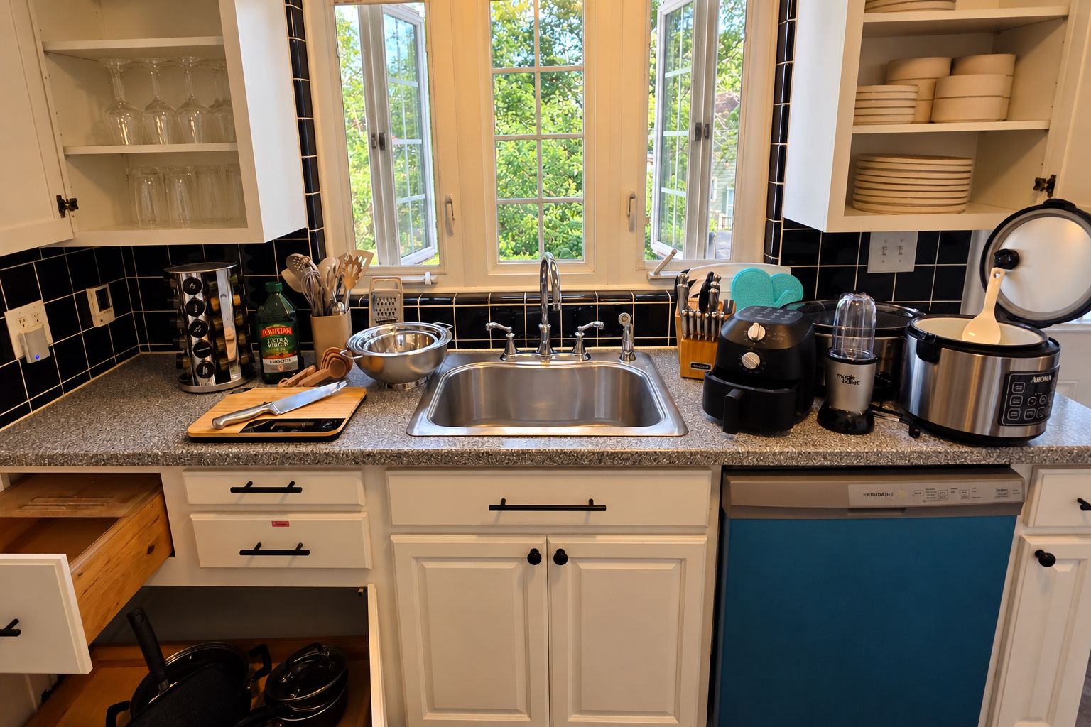 A kitchen with a stainless steel sink, a toaster, a slow cooker, and a dish rack.