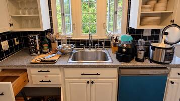 A kitchen with a stainless steel sink, a toaster, a slow cooker, and a dish rack.