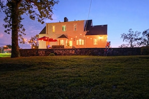 A two-story house with a stone wall in front, a red umbrella, and string lights.