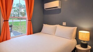 A bedroom with a bed, an air conditioning unit, a lamp, and curtains. - Coastal Home | Patio & Firepit | Backyard Games (Merrillville)