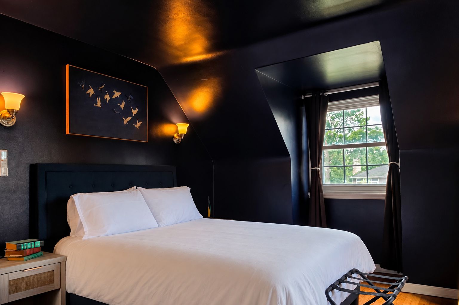 A bedroom with a bed, bedside lamps, a window, and a wall-mounted artwork.