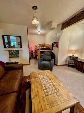 A living room with a brown leather sofa, a wooden coffee table with a mosaic top, a gray armchair, and a wooden bookshelf. - Cozy Cedar Cabin w/ Hot Tub, Mountain Views + Fireplace > Open Sky Cabin, CO (Jefferson)