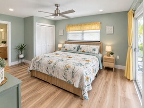 Ein Schlafzimmer mit Bett, Nachttischen, Deckenventilator, Fenster mit Jalousien und einer Tür mit Schrank.