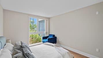 A bedroom with a bed, a blue chair, a window, and a view of greenery outside.