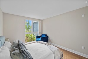 A bedroom with a bed, a blue chair, a window, and a view of greenery outside.