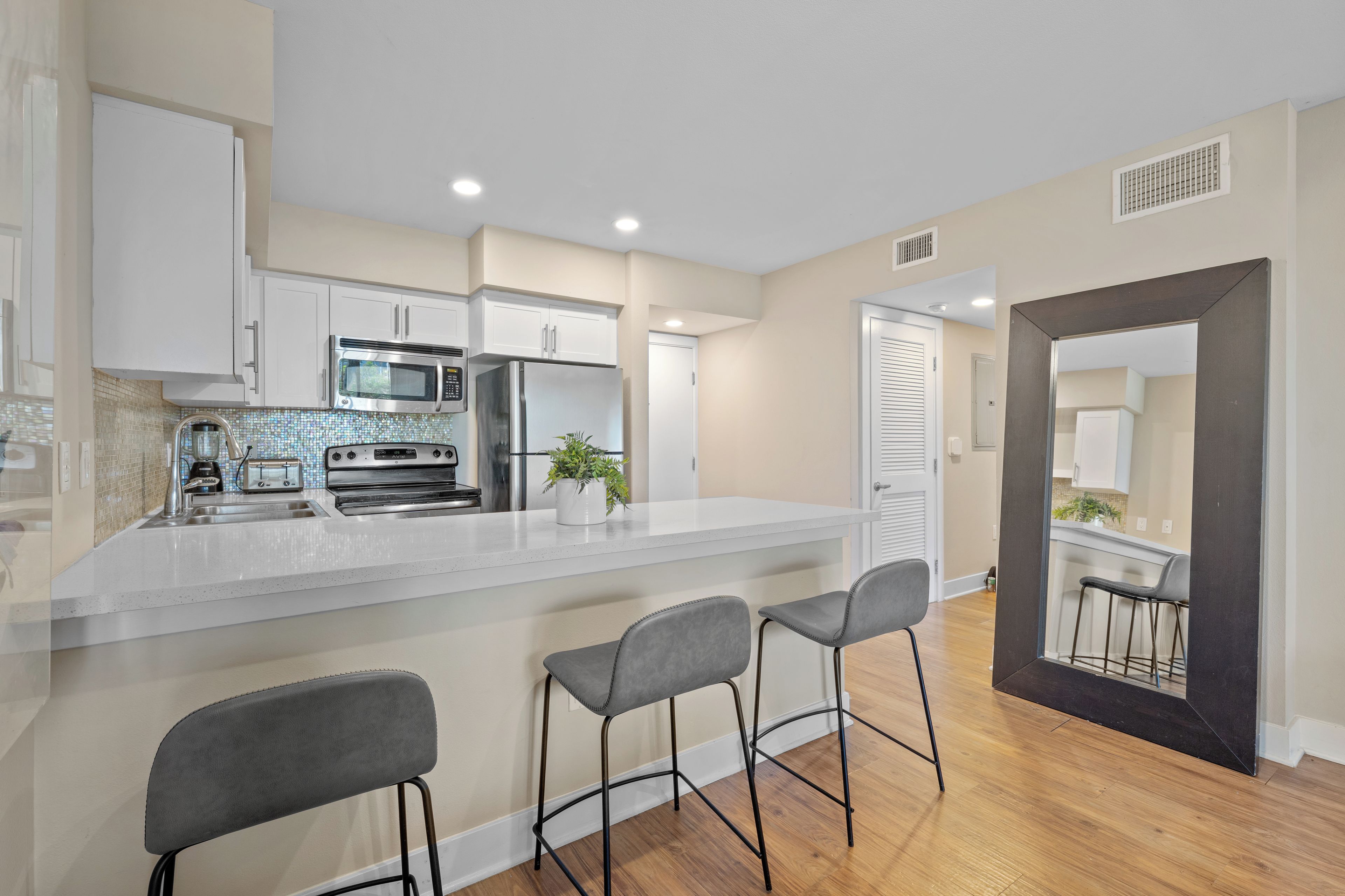A modern kitchen with a central island, bar stools, and a view into the dining area.