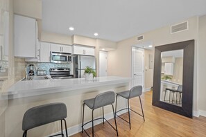 A modern kitchen with a central island, bar stools, and a view into the dining area.