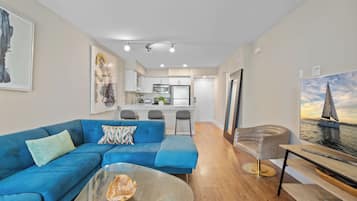 A modern living room with a blue sofa, a glass coffee table, and a painting of a sailboat.