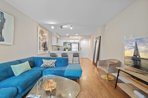 A modern living room with a blue sofa, a glass coffee table, and a painting of a sailboat.