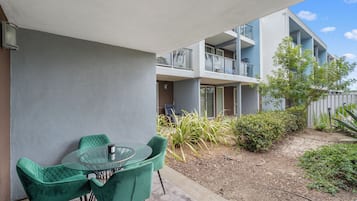Ein Balkon mit Glastisch und Stühlen, Blick auf ein Gebäude mit Balkonen und etwas Grün.