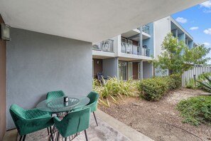 Un balcon avec une table et des chaises en verre, une vue sur un immeuble doté de balcons, et quelques plantes.