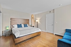 A hotel room with a wooden bed, a blue chair, a lamp, and a surfboard.
