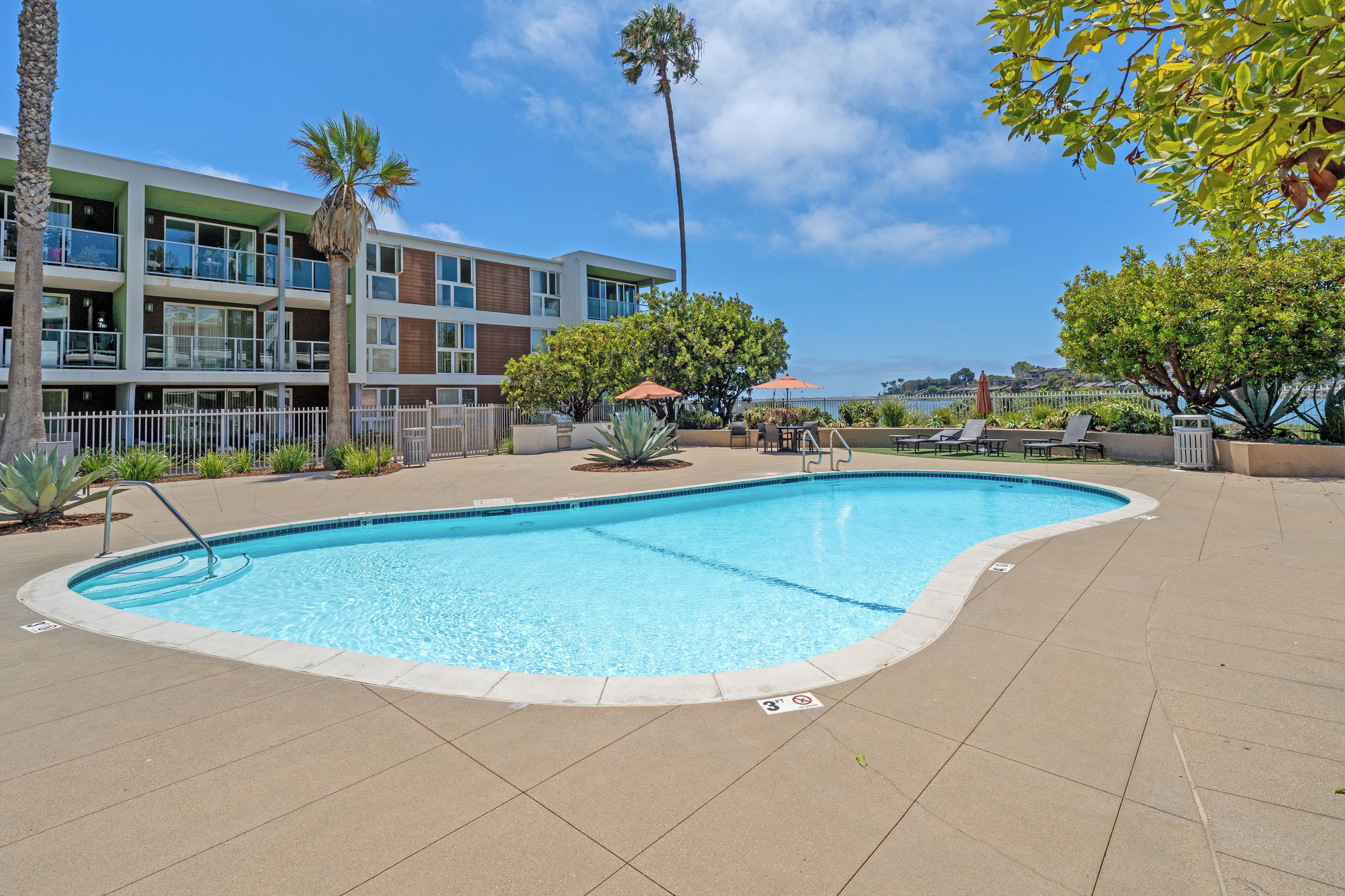A swimming pool with a tiled edge, surrounded by a paved area with lounge chairs and umbrellas.