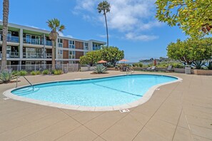 A swimming pool with a tiled edge, surrounded by a paved area with lounge chairs and umbrellas. - Del Mar Direct access to the main channel Water View, Pool, jacuzzi and Gym (Marina del Rey)