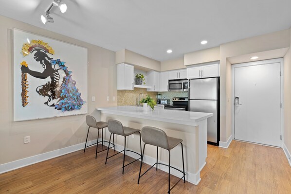 A modern kitchen with a central island, bar stools, and a decorative wall piece.