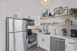 A modern kitchen with stainless steel appliances, white cabinetry, and decorative items on shelves. - ~NEW~ Exclusive Beach Loft ~Turtle Bay Golf Course (Kahuku)