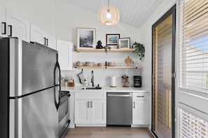Eine moderne Küche mit weißen Schränken, einem Edelstahlkühlschrank, einer Spülmaschine und einer Pendelleuchte.