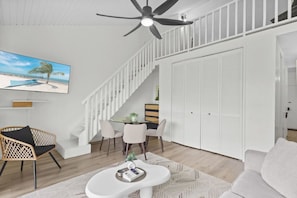Ein modernes Wohnzimmer mit Essbereich, Deckenventilator, Fernseher und einer Treppe, die zu einer oberen Ebene führt.