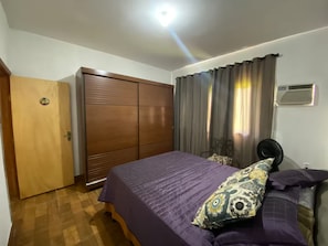 A bedroom with a bed, a wardrobe, a fan, and a window with curtains.