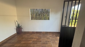 A room with a tiled floor, a window with vertical blinds, a potted plant, and a door with a metal gate.