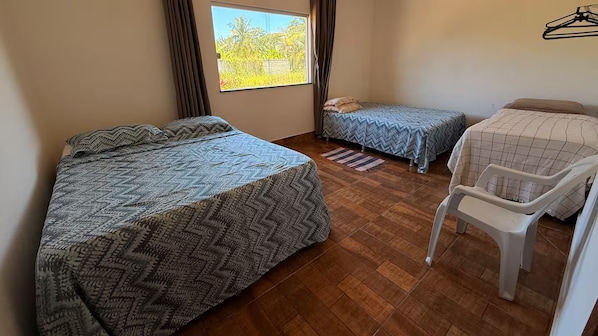 A room with two beds, a chair, and a window with a view of greenery. - Casa Mar e Sol beachfront in Coroa Vermelha (Santa Cruz Cabrália)